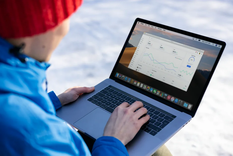 Person analyzes stock data with a smartphone and laptop, indoors.